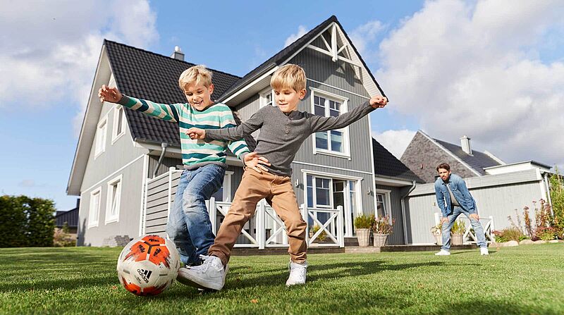 Hausbau planen, zwei Jungs spielen Fußball vor Einfamilienhaus