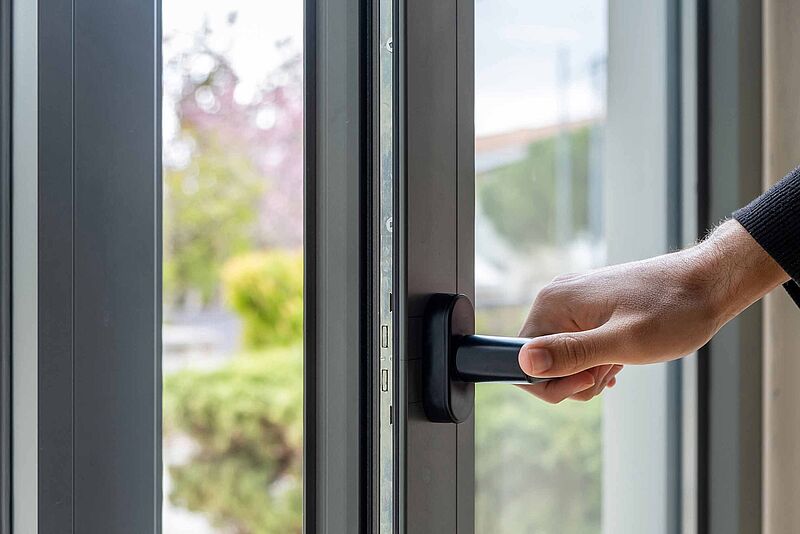 Eine Person öffnet ein schwarzes Alluminiumfenster und lässt frische Luft in den Raum